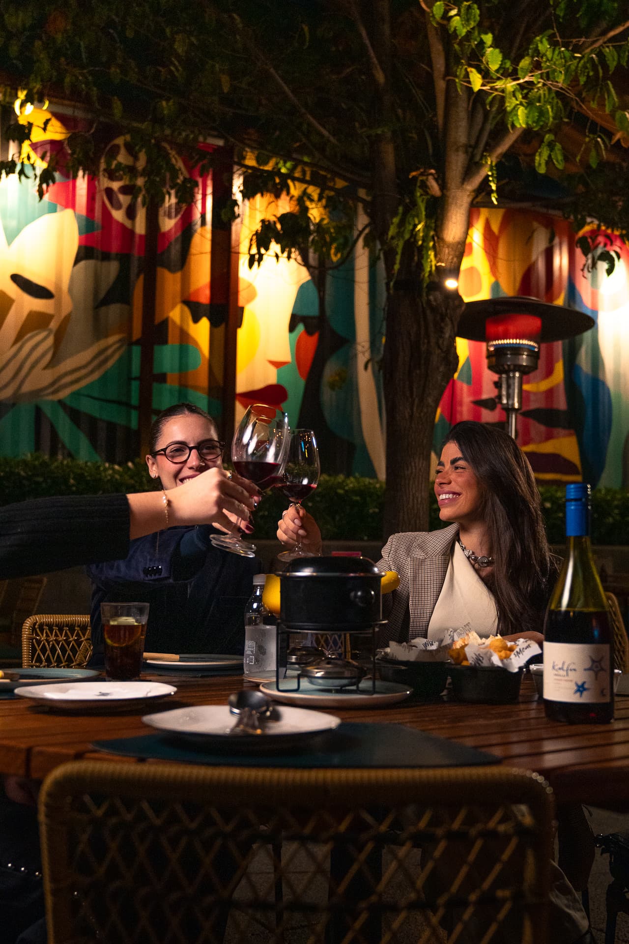 Amigos brindando com vinho numa mesa da área externa do Smeat à noite